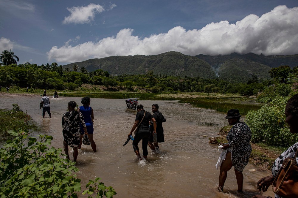People cross a river during a funeral procession for a person who died during the earthquake, in L'Asile, Haiti, on Aug. 18.