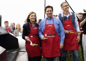 From left, Iowa Gov. Kim Reynolds, Florida Gov. Ron DeSantis and Rep. Randy Feenstra flip meat on the grill for a photo op during the annual Feenstra Family Picnic at the Dean Family Classic Car Museum in Sioux Center, Iowa, on Saturday, May 13, 2023. (Photo by Rebecca S. Gratz for The Washington Post)