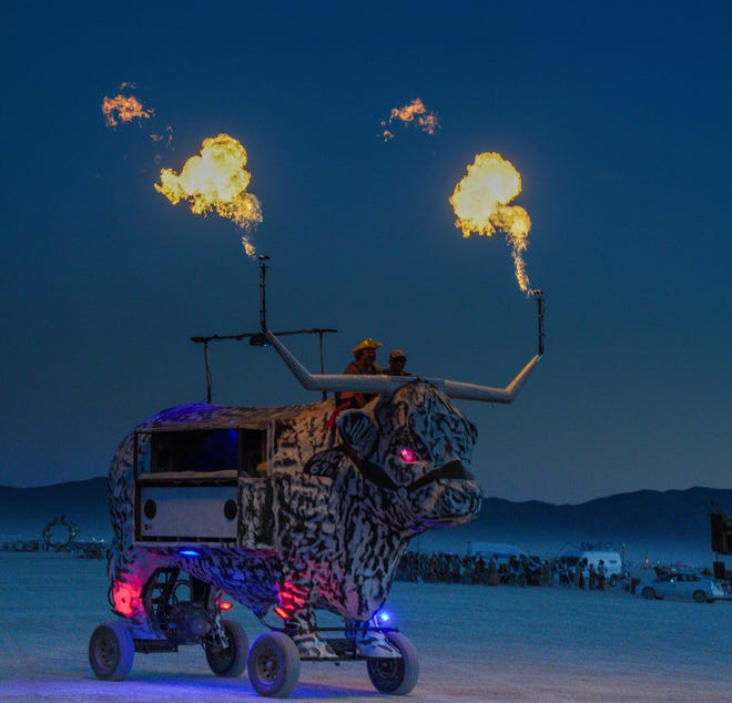A mobile steer shoots flames from its horns at Burning Man as night falls.