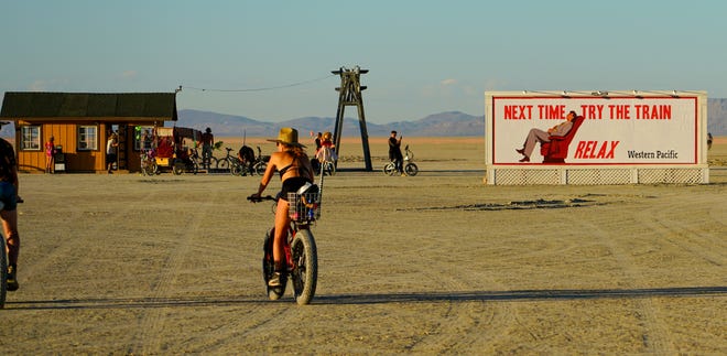 A Burning Man attendee rides their bike toward a train station built in the middle of the desert.
