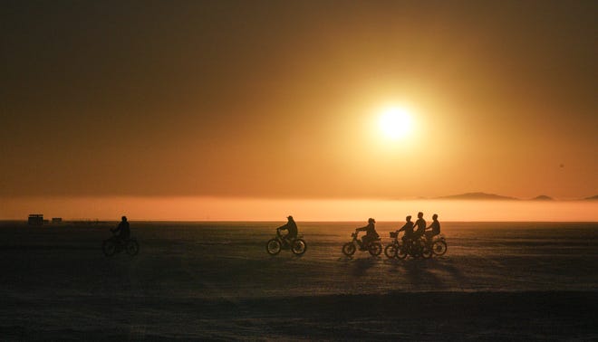 Burning Man attendees ride across the Black Rock Desert at sunrise.
