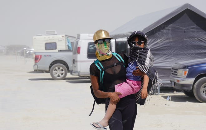 Tracie Williams of Portland carries her son, known at Burning Man as "Pool Boi 01" during a dust storm at the event. Williams, a volunteer with a group that helps participants having a bad emotional reaction to their Burning Man experience, said she has been surprised at how easy it's been to have her son with her.