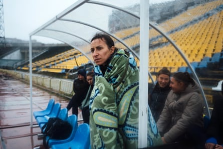 Yana Vynorukova, Mariupol’s president, watches from the dugout in a blanket.