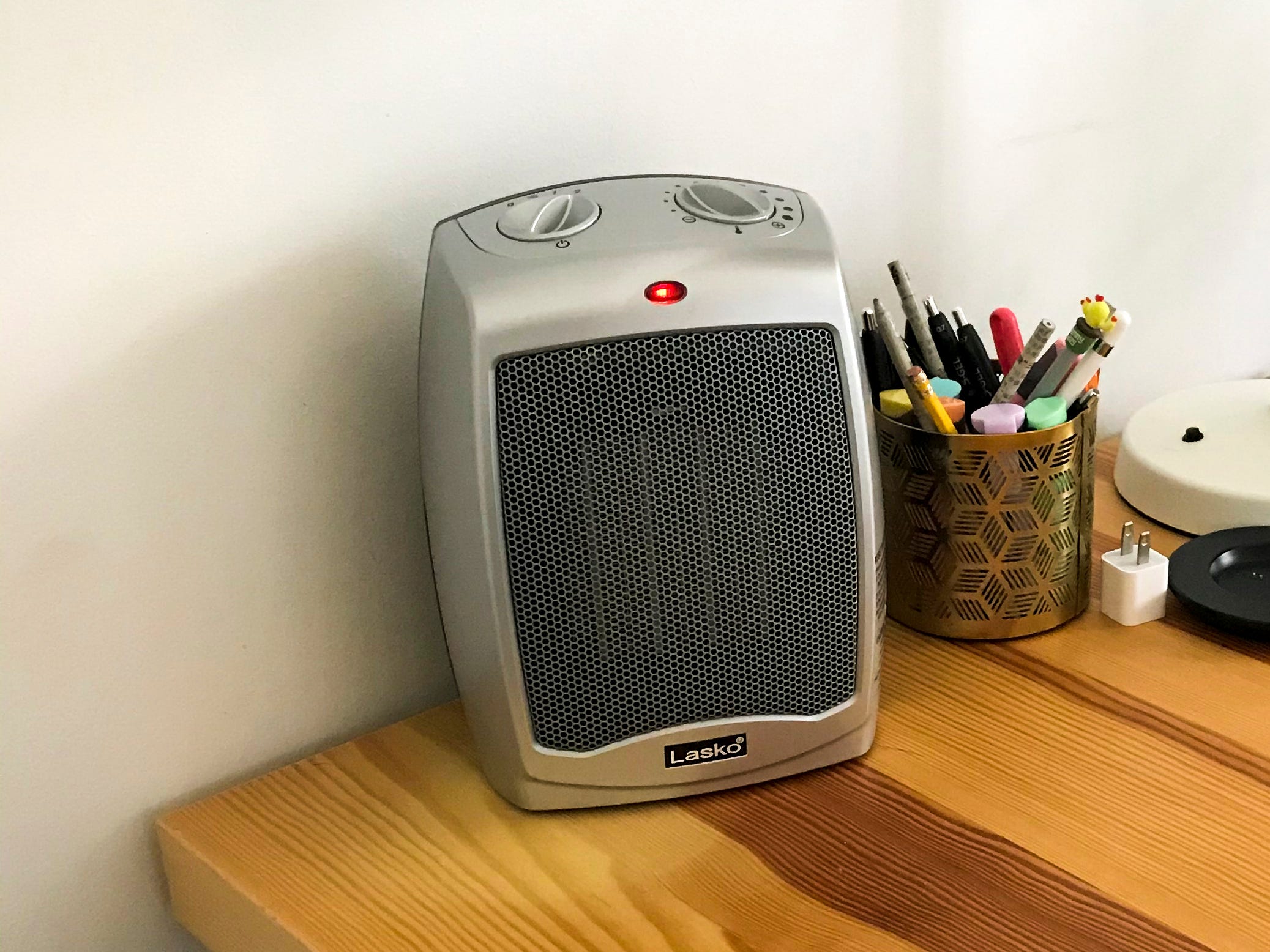 The Lasko 754200 Ceramic Portable Space Heater, the best space heater overall in 2022, is displayed on a wood table next to a container of writing tools.