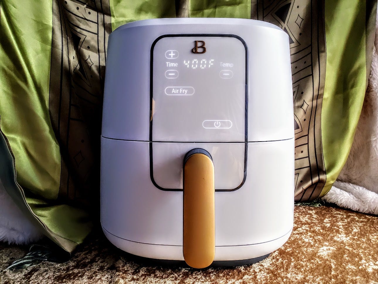 The Beautiful 6 Quart Touchscreen Air Fryer by Drew Barrymore is displayed with a green and gold background.