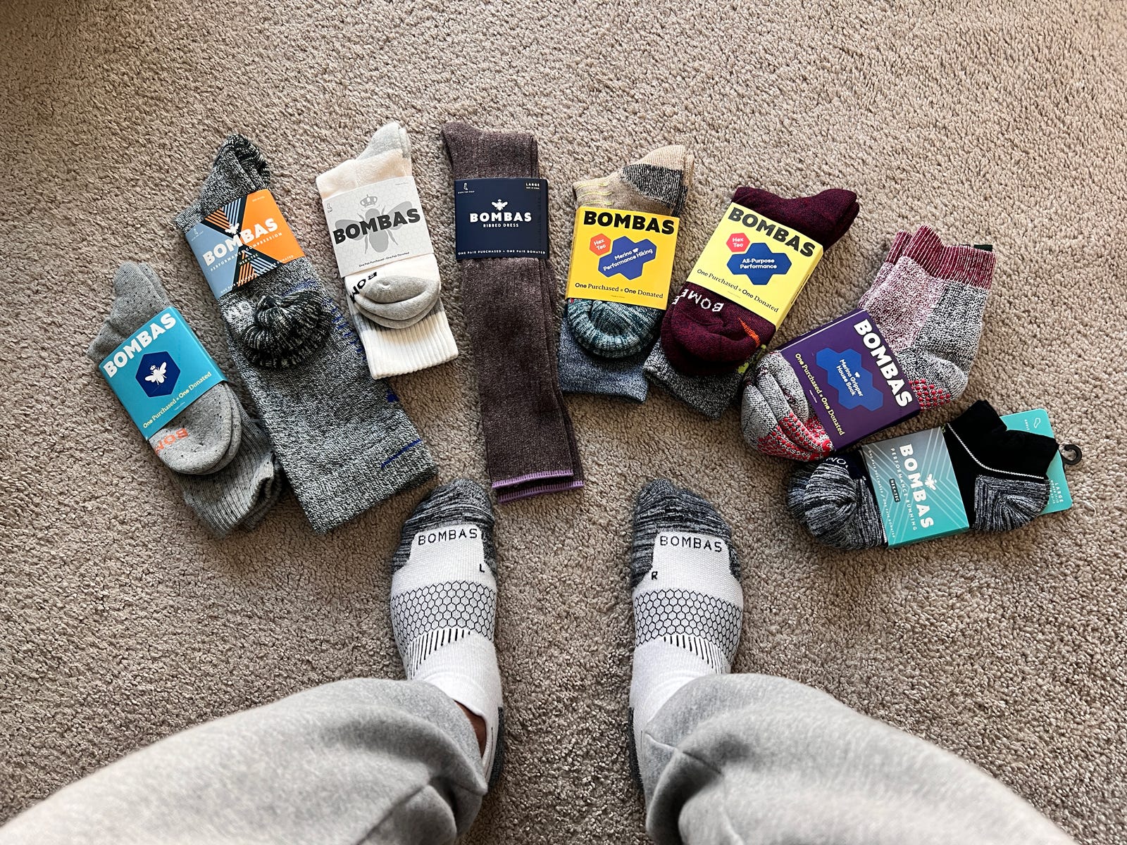 A man wearing Bombas socks with a collection of Bombas socks laid out on the floor around his feet.