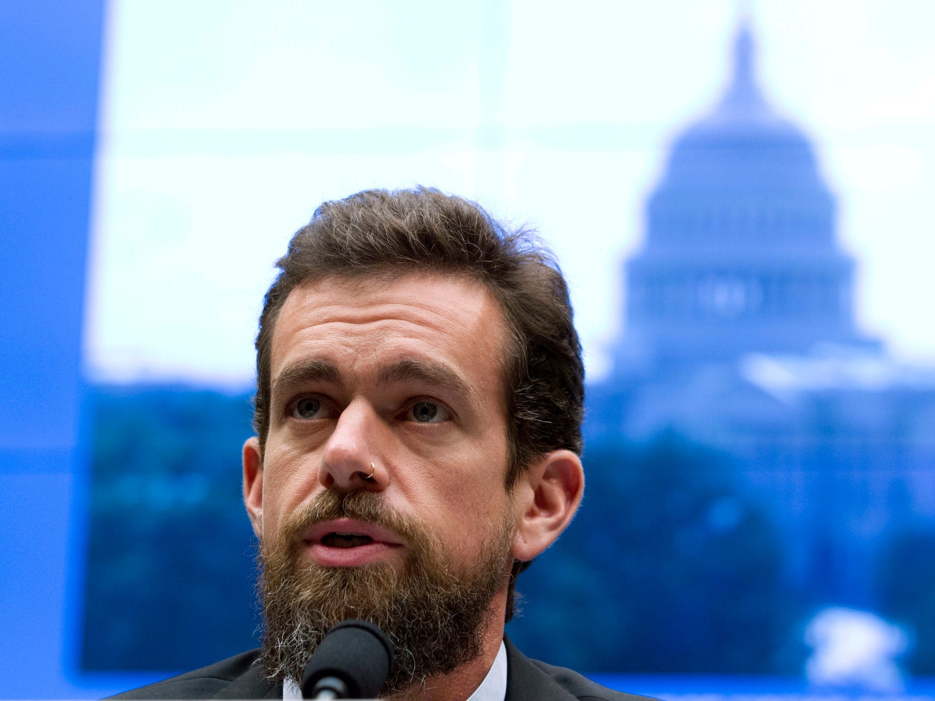 Jack Dorsey speaking into a microphone with a blue scene in the background.