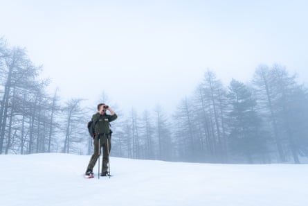A park ranger looks through binoculars in a snowy landscape