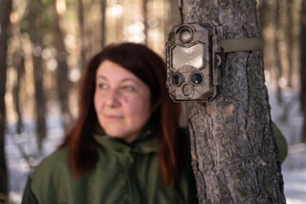 A woman next to a camera trap fixed to a tree trunk