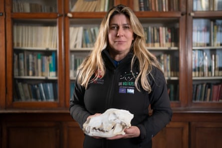 A woman holds a wolf skull in front of a glass-fronted bookcase