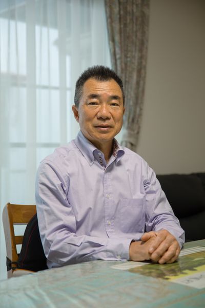 A photo of Mitsuyoshi Hirai, the former chief engineer of the Ocean Link. He sits at a table, his hands folded on a chart.