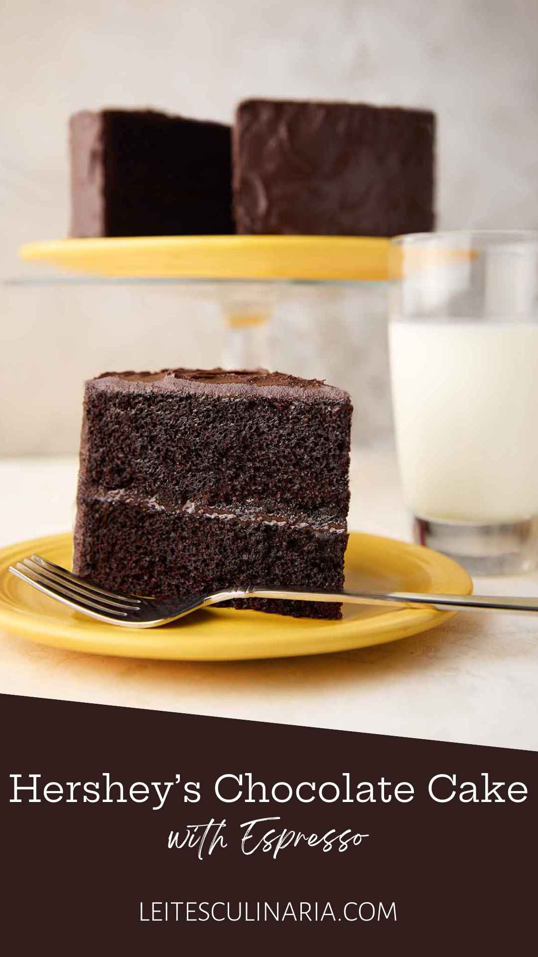 A slice of Hershey's chocolate cake with chocolate frosting on a yellow plate, with the remaining cake on a stand in the background.