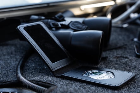 An open leather wallet with a silver shield badge inside it sits next to a pair of bioculars.