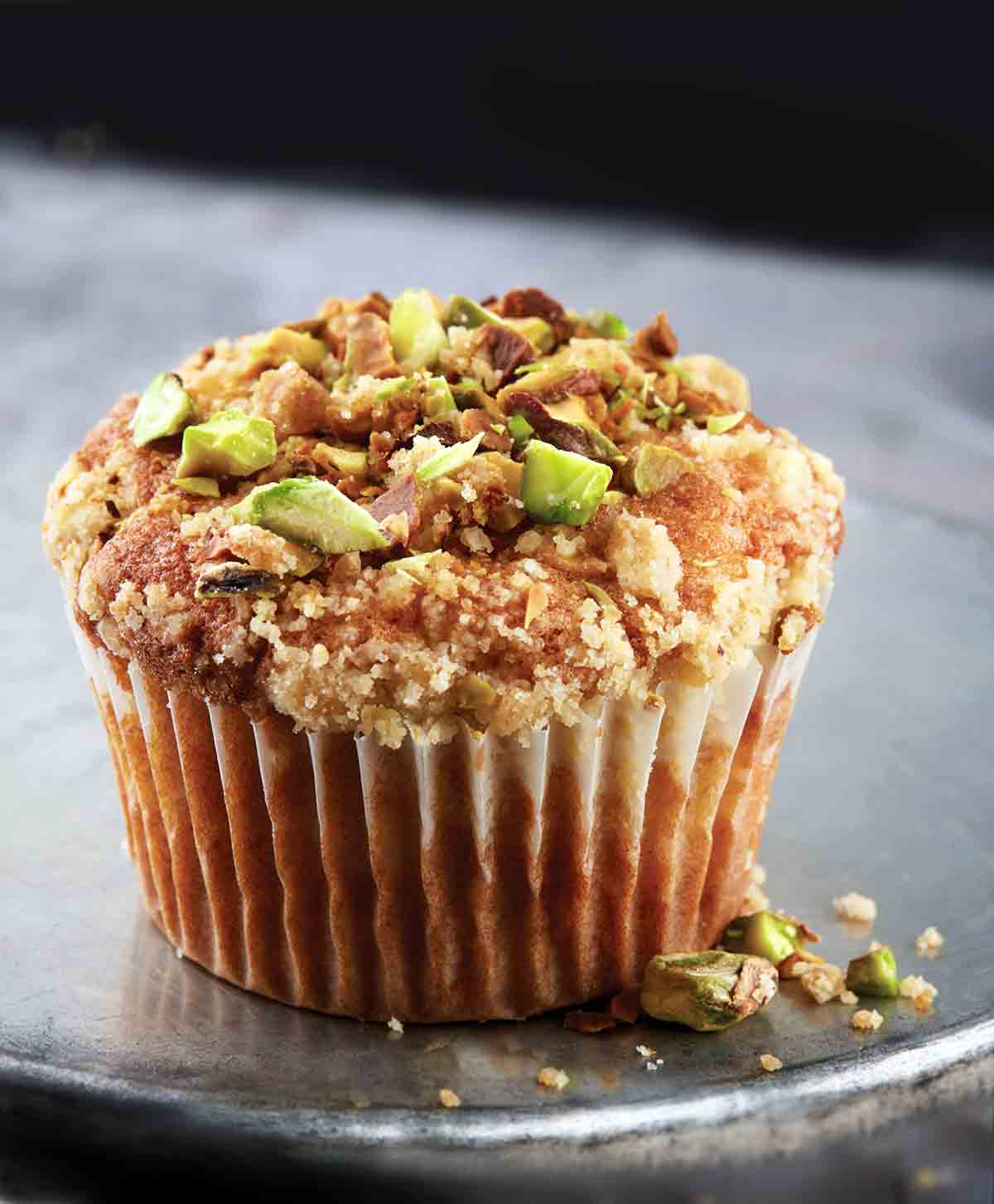 A single apple spice muffin with streusel and pistachios on an inverted metal cake tin.