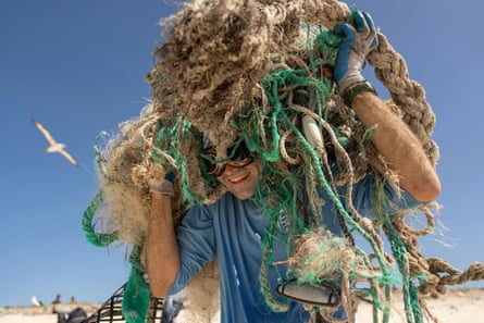 A man carries marine debris across a beach