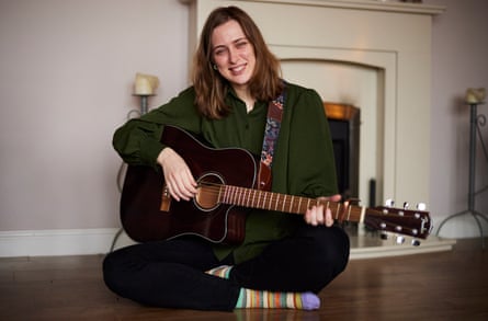 Natacha sits on the floor playing her guitar. 