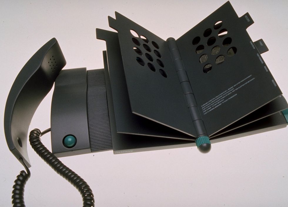 Photo of an electronic device consisting of a landline phone handset connected to a booklike object with several hard plastic pages.