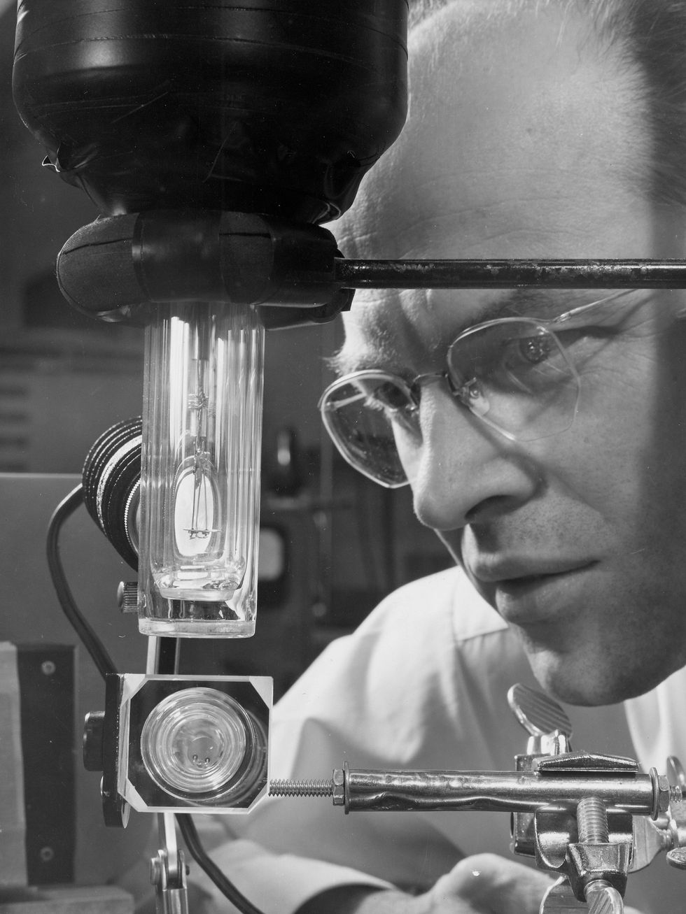 A photo of a man in glasses looking at a glass container.