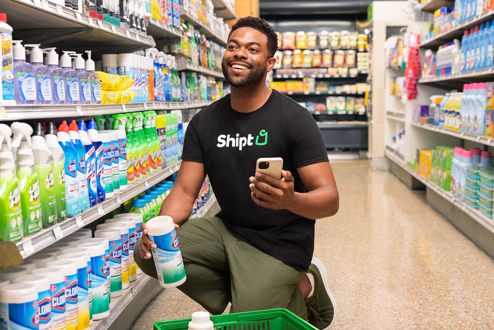 A photo of a smiling man kneeling in a cleaning aisle of a store.  