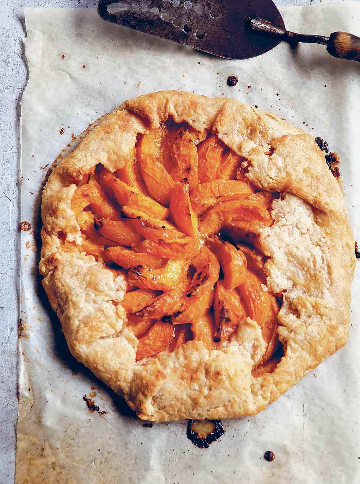 A cooked apricot galette on a piece of parchment paper with a metal spatula beside it.