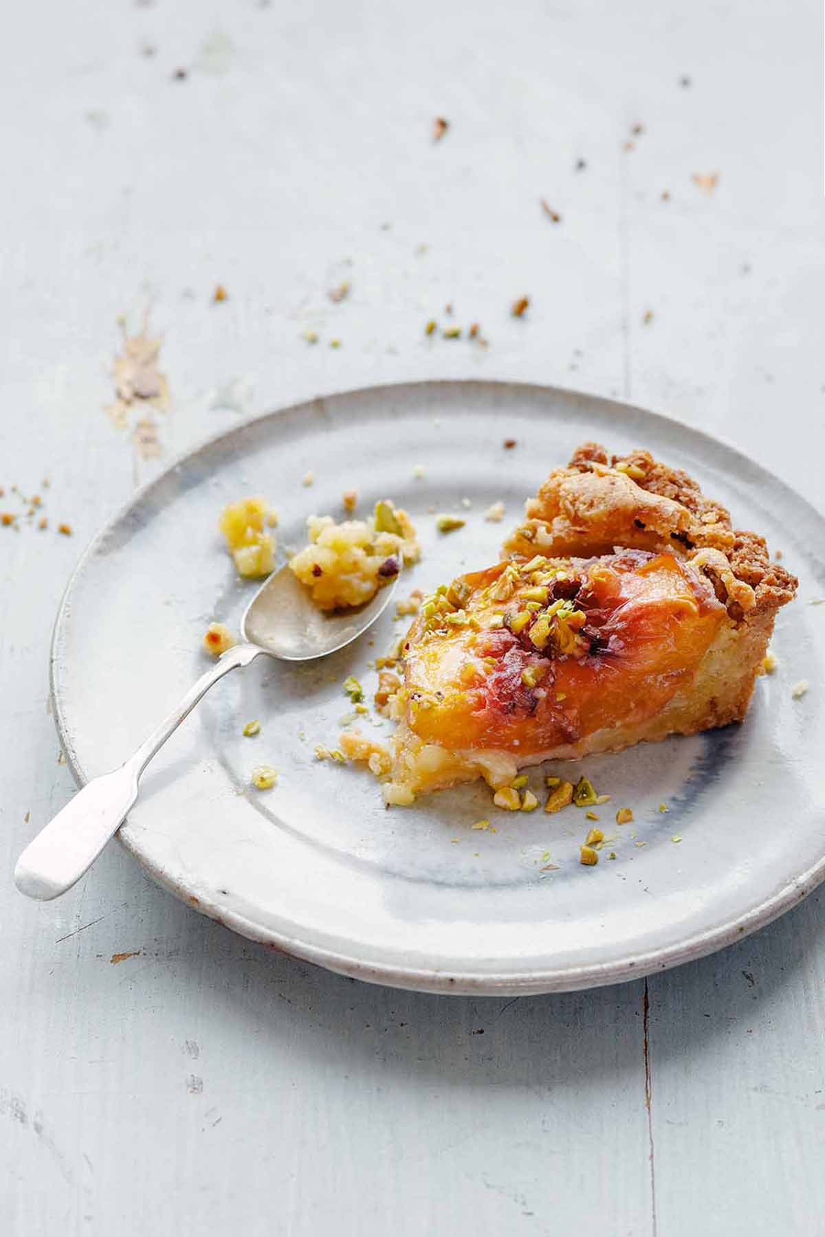 Plate with an slice of apricot tart filled with frangipane and topped with chopped pistachios.