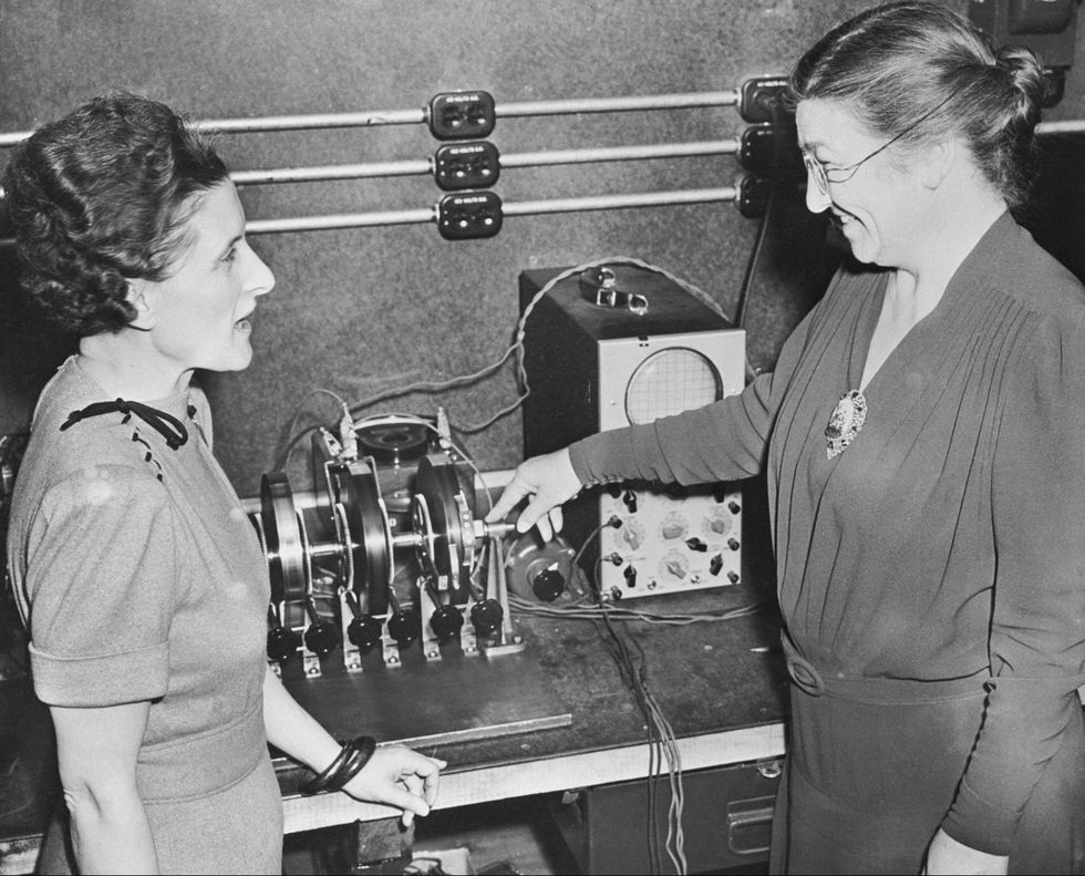 black and white photograph of two women talking and smiling with hands on a desk