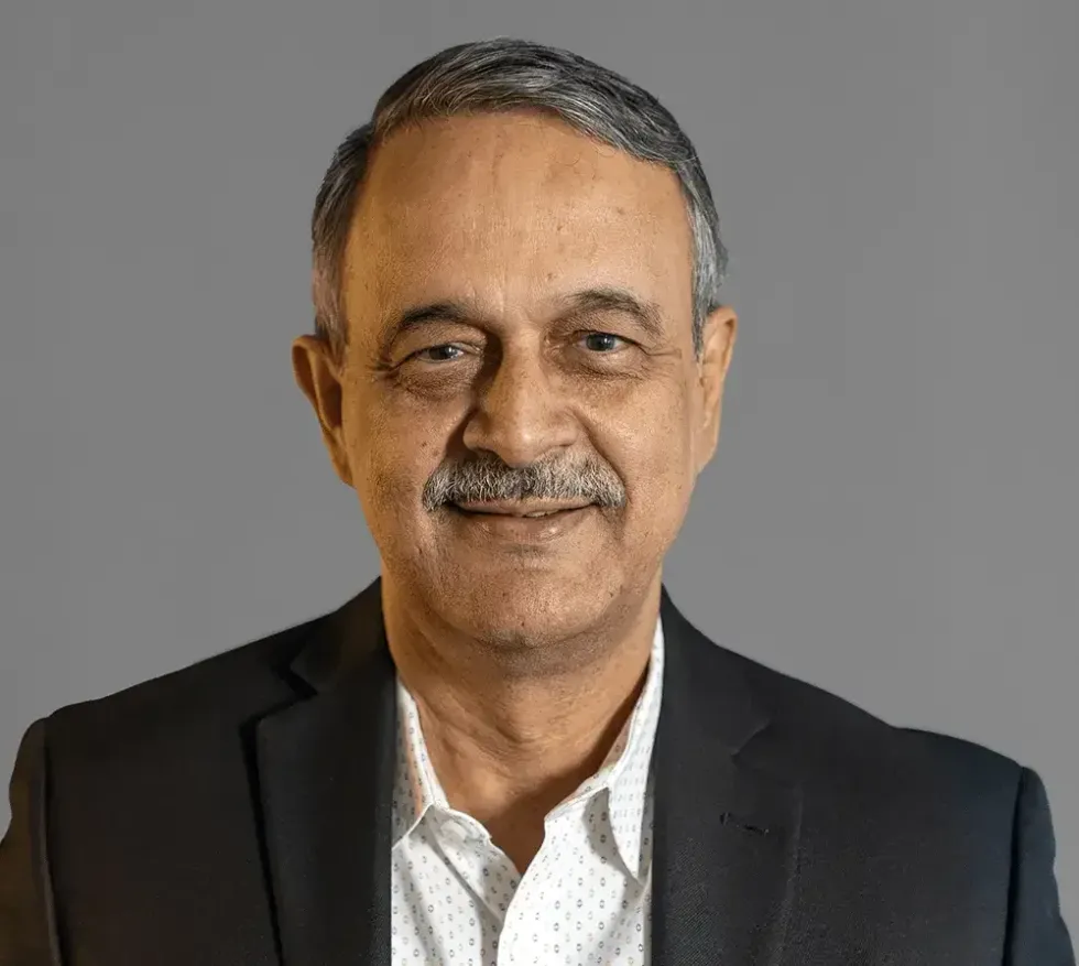 man smiling for a portrait in a suit jacket and white shirt  against a gray background