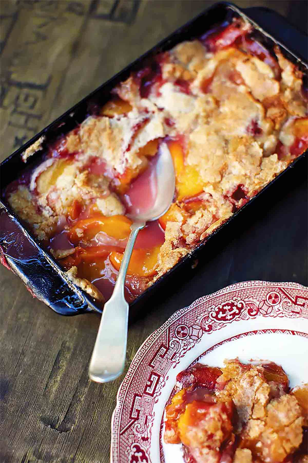 A spoon resting in a dish of cornmeal drop-biscuit peach cobbler.