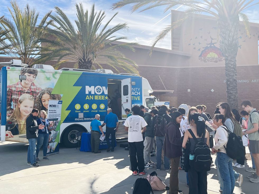 outdoor view of a truck with text on it with a line of students waiting next to it