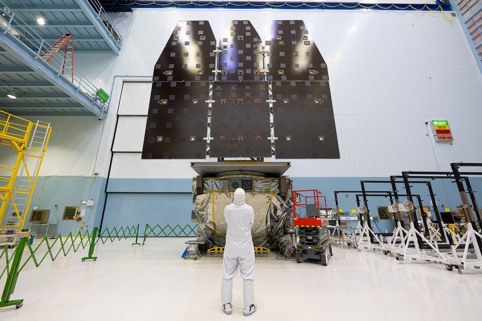 Photo of three large flat black panels that are connected and raised on a lift, with a person in a cleanroom suit looking up at them.