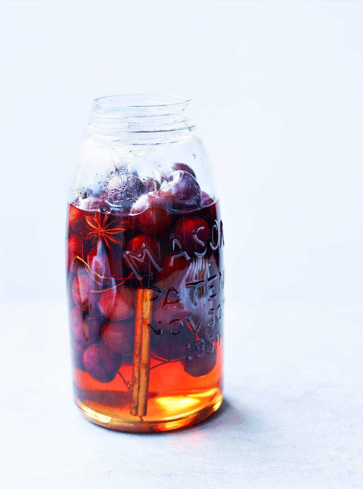 A mason jar mostly filled with pickled cherries, pickling liquid, star anise, and a cinnamon stick.