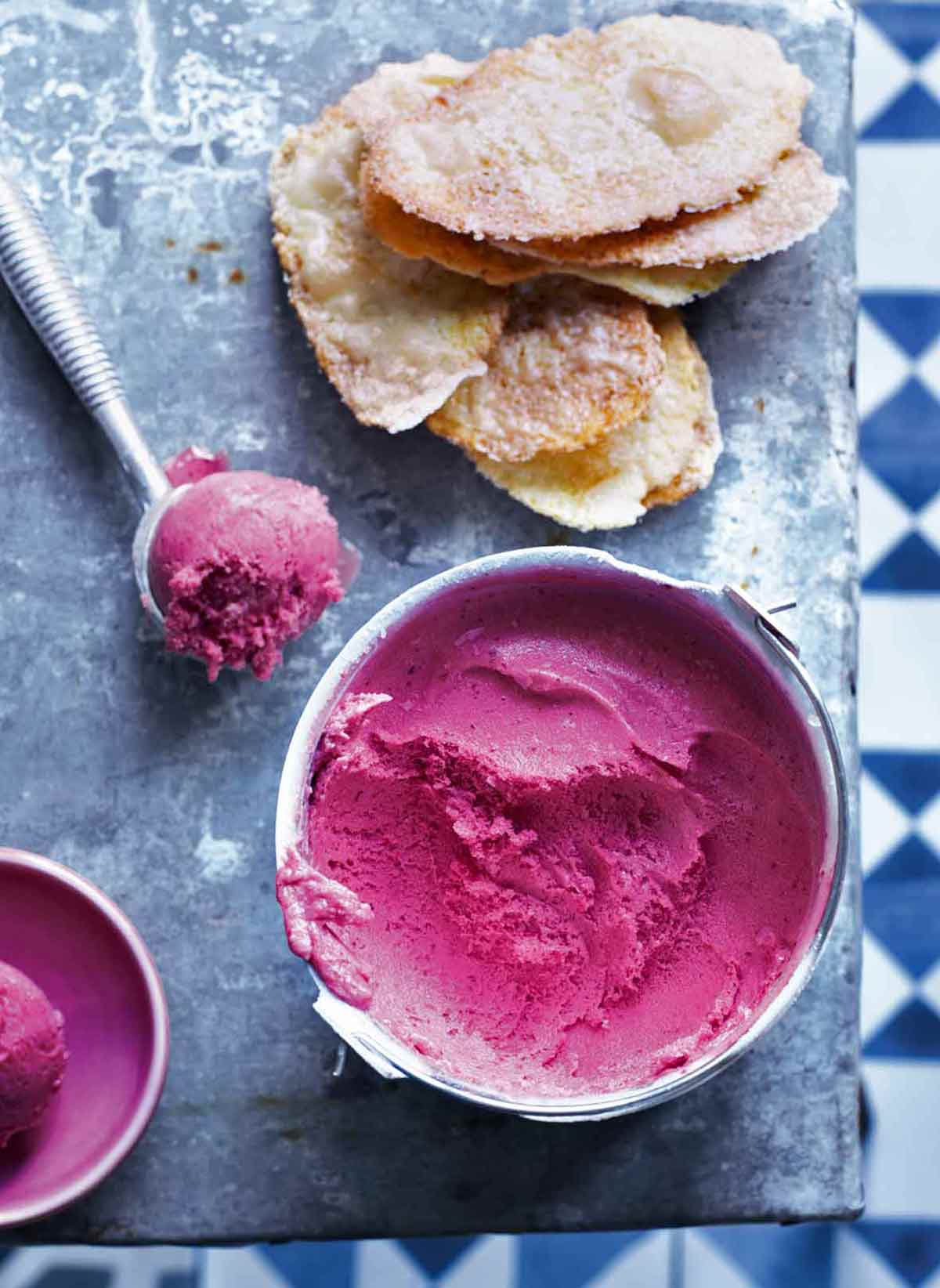 A frozen tub of plum sorbet, with a scoop of sorbet and some sugar cookies lying beside it.