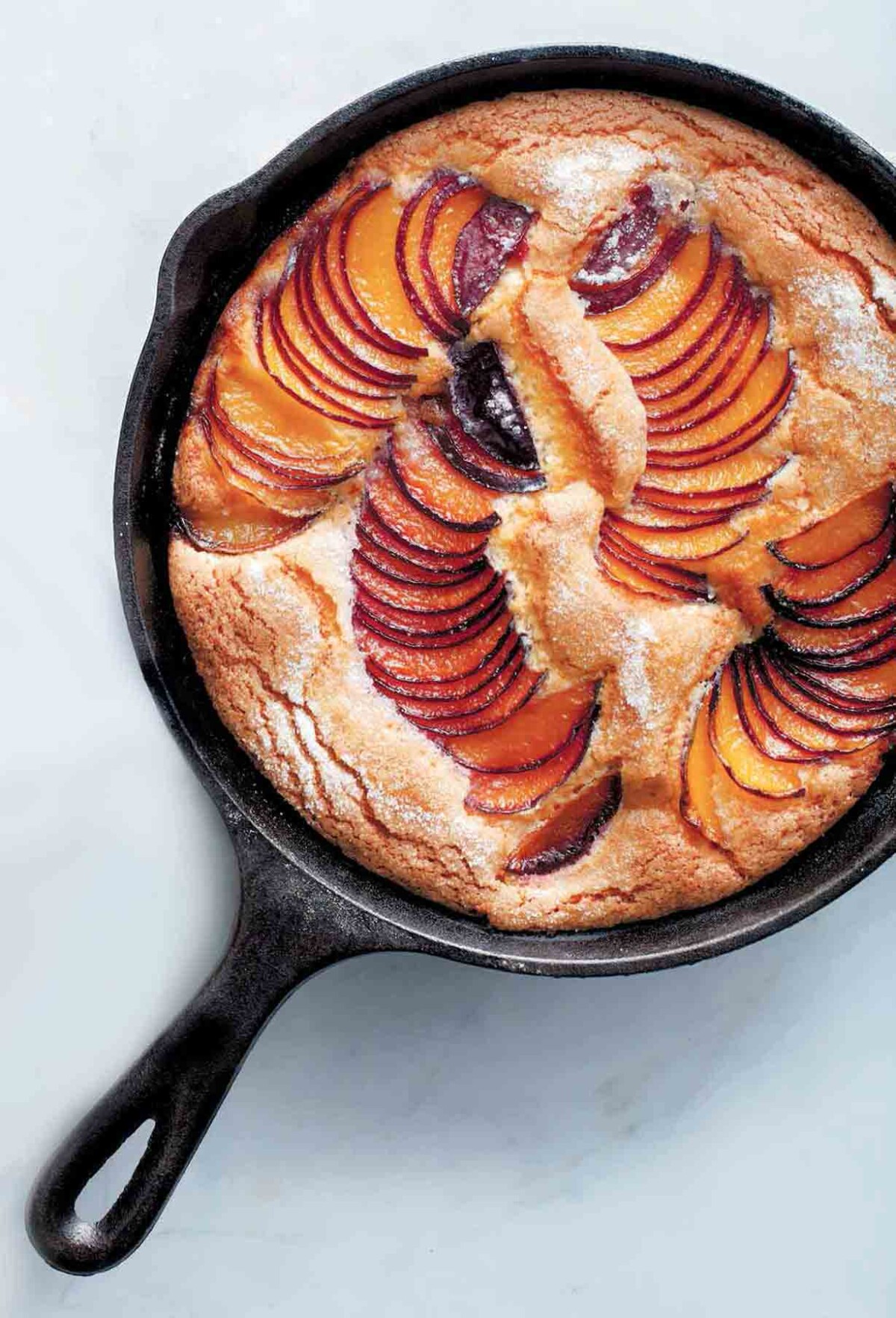 A cast-iron skillet plum cake with slices of fanned out plums baked in