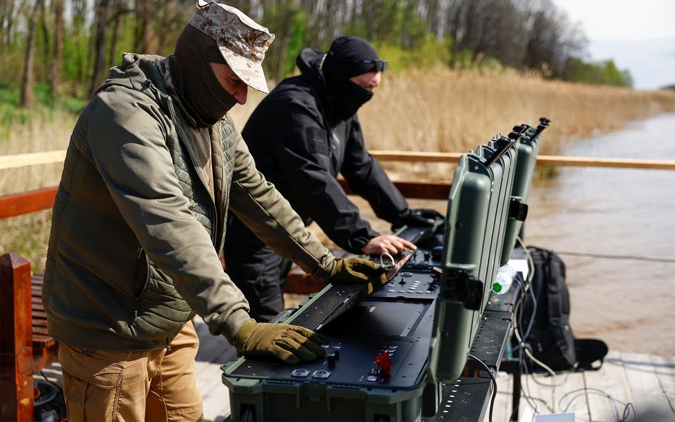 Two men wearing balaclavas operate suitcase-style terminals for remote control of sea drones. 