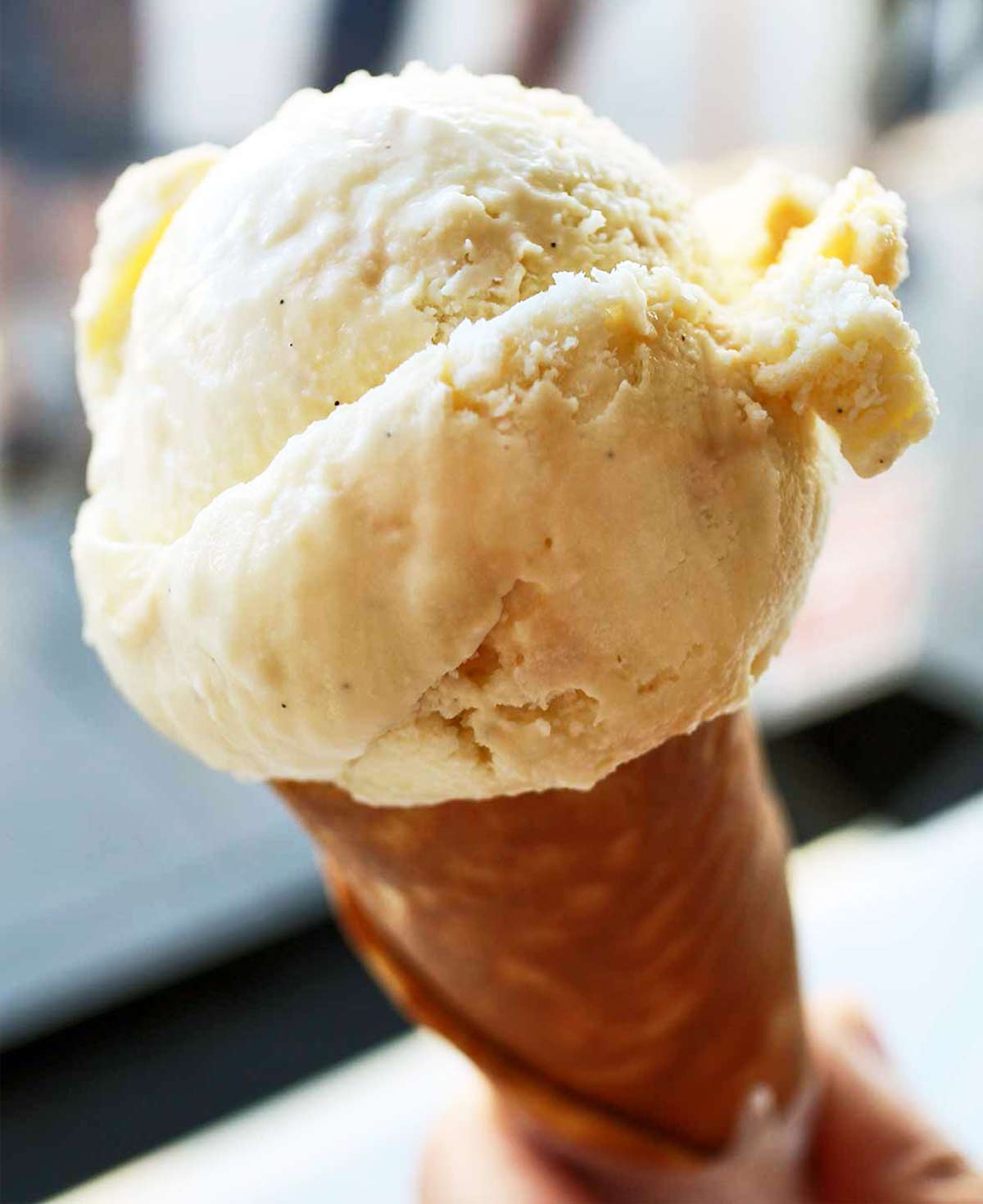 A person holding an ice cream cone filled with rich vanilla ice cream.