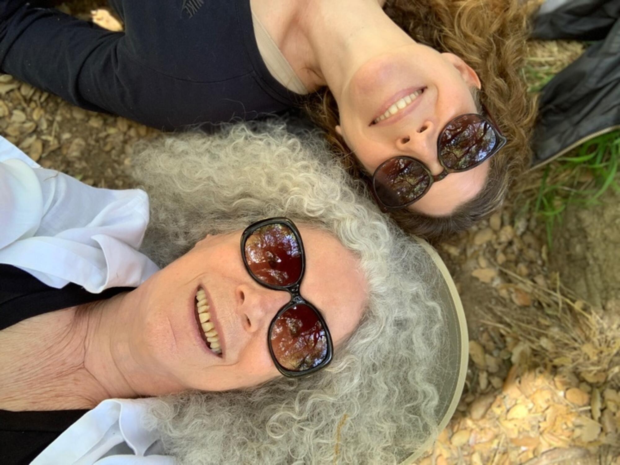 Two women wearing sunglasses and lying on their backs on the ground