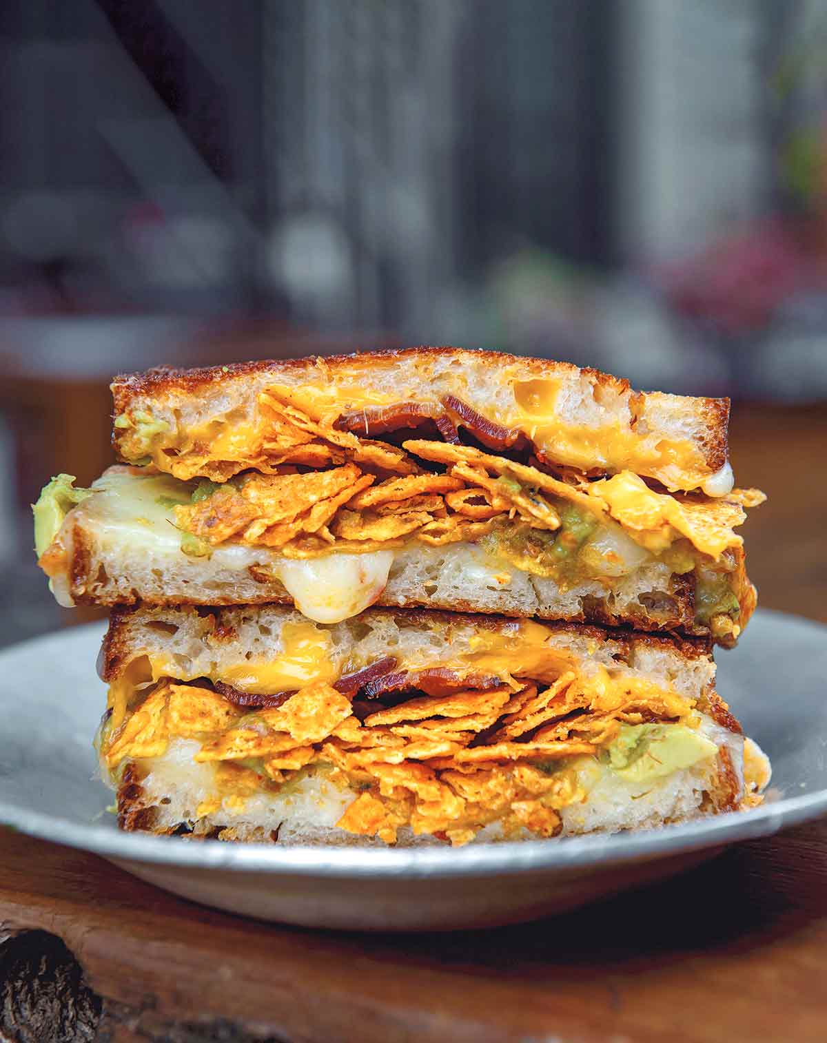 A gray plate with a grilled cheese with Doritos, bacon, and guacamole.