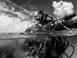 Black and white photograph of two people pulling up fishing debris onto a boat.