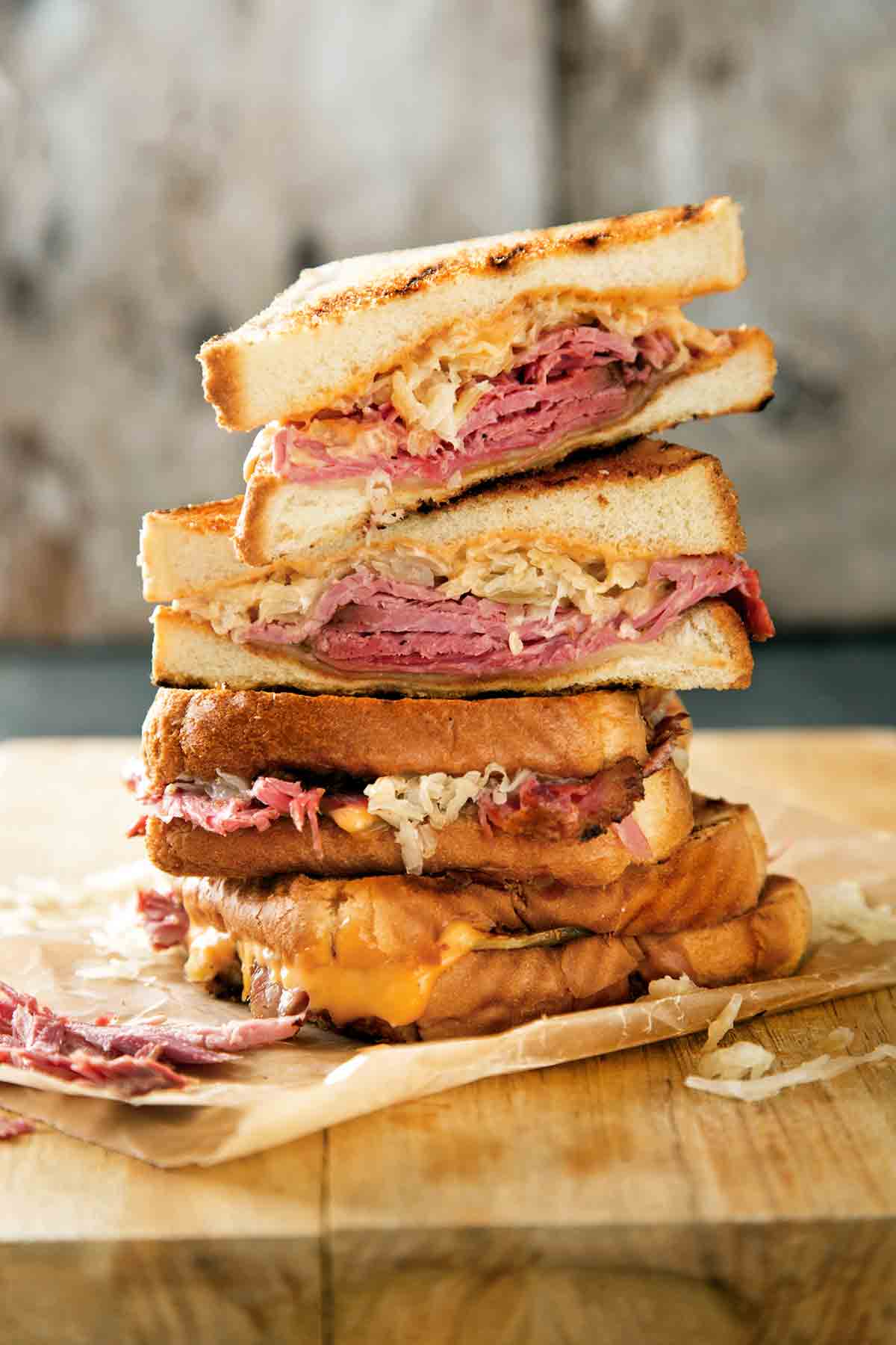 A stack of halved reuben sandwiches on a wooden cutting board.