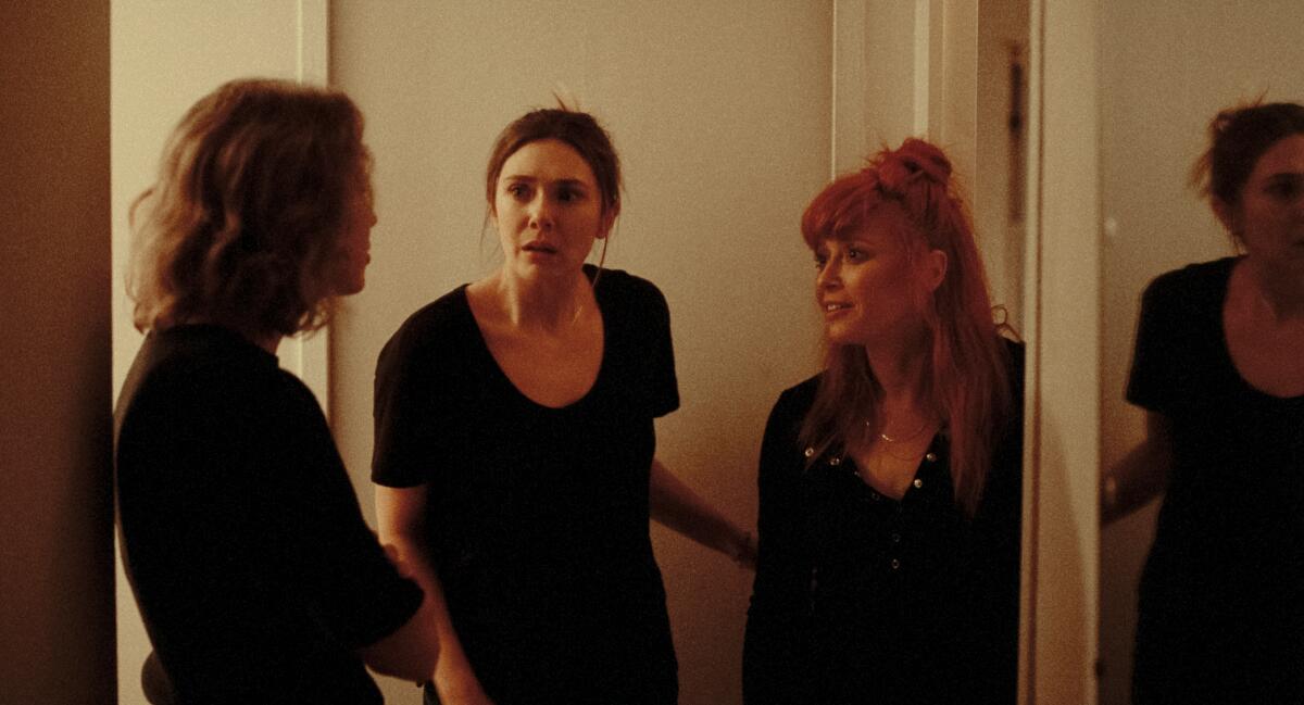 Three women have a discussion in a hallway.