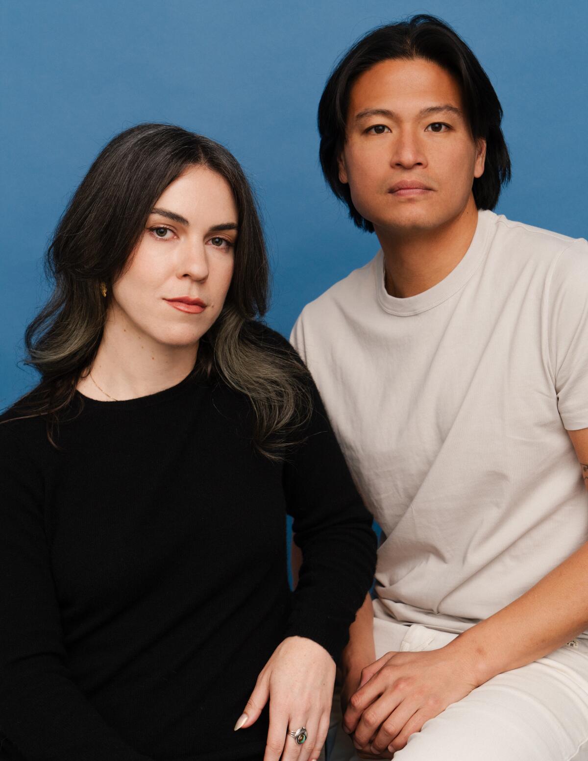 Kate Conger and Ryan Mac sit in front of a blue background and look into the camera.