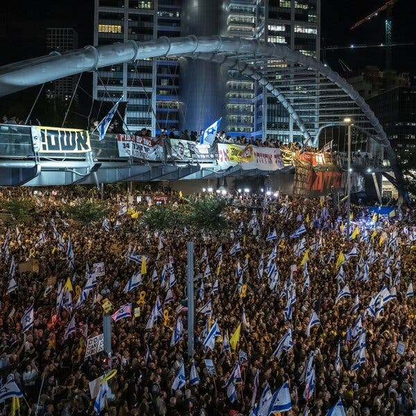 A large crowd in an open city space at night. Many people are carrying blue-and-white Israeli flags.