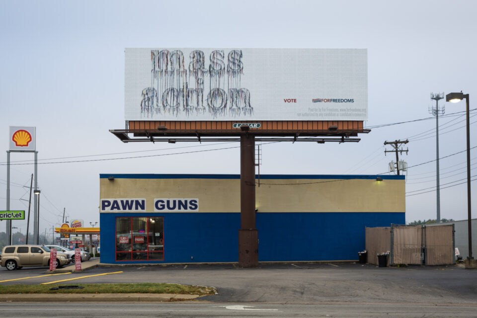 a billboard sign outside of a pawn shop for guns reads, "mass action. vote."