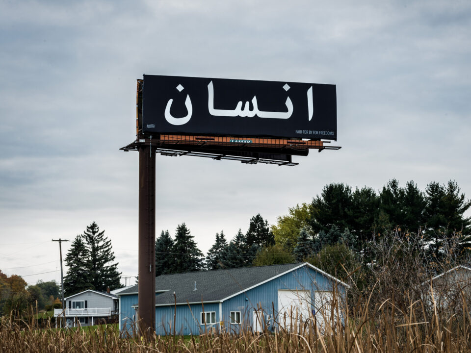 a black billboard with white text reading, "human being" in Arabic