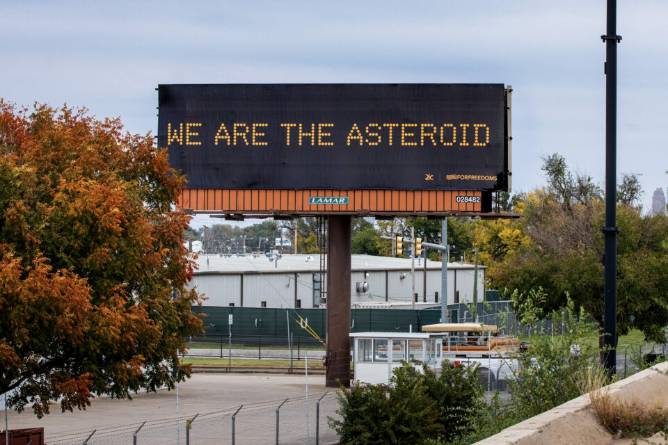 a billboard reading, "WE ARE THE ASTEROID" in the style of a traffic control sign