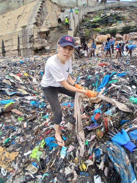 Fleur pulls an item of clothing from a pile of waste clothing that encompasses an entire beach.