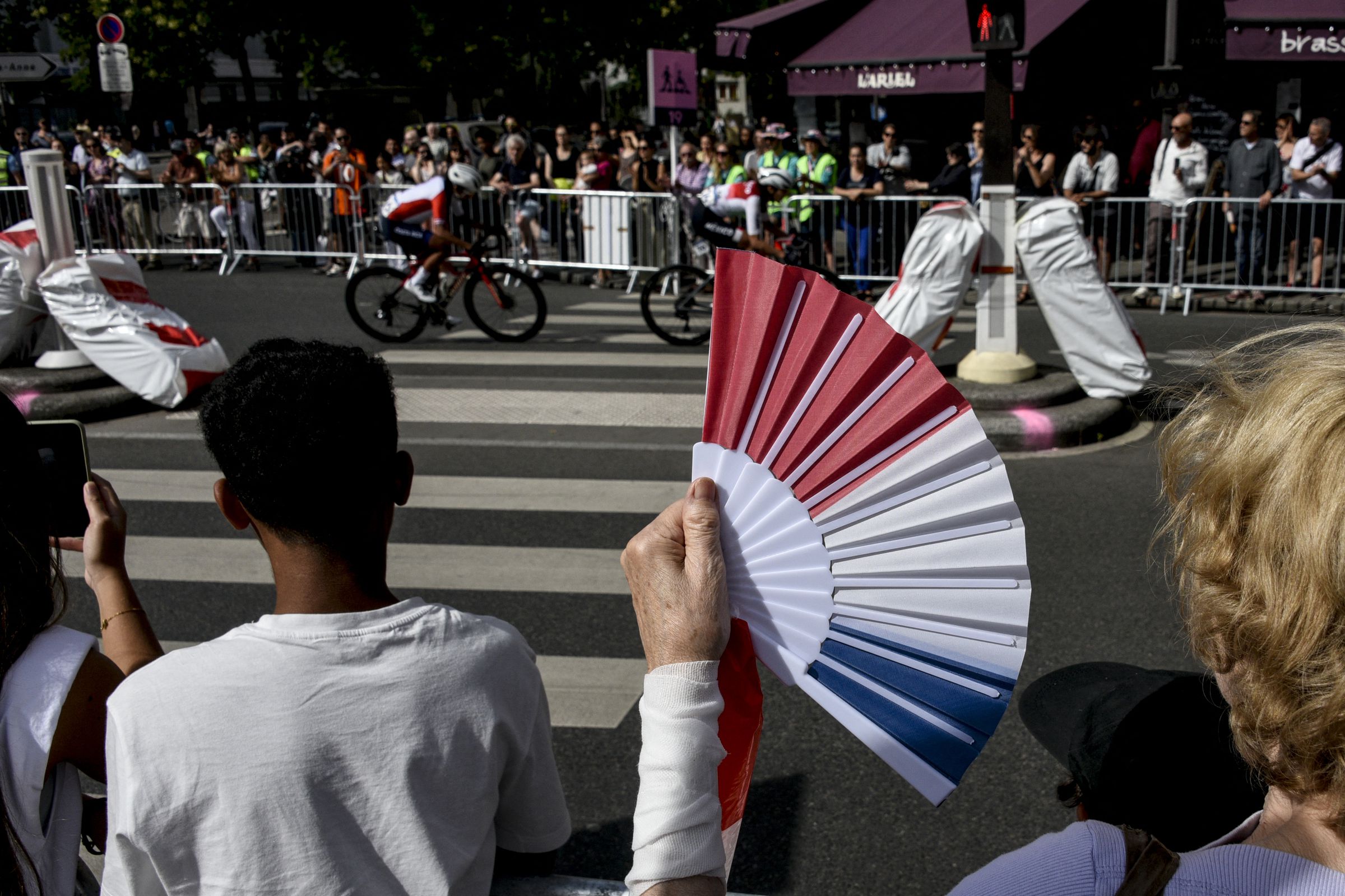 A spectator holds up a fan while watching bikers pass by on the street.