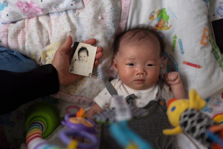 Michaela Dietz, an adoptee from South Korea, holds a baby photo of Robyn Joy Park next to Park's newborn daughter, Rae