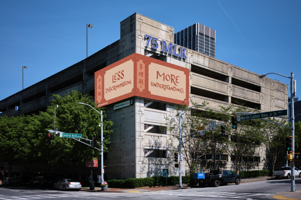 a two-sided billboard folding over the corner of a building that reads, "Less Discrimination, More Understanding" in stereotypical "Chop Suey" Font