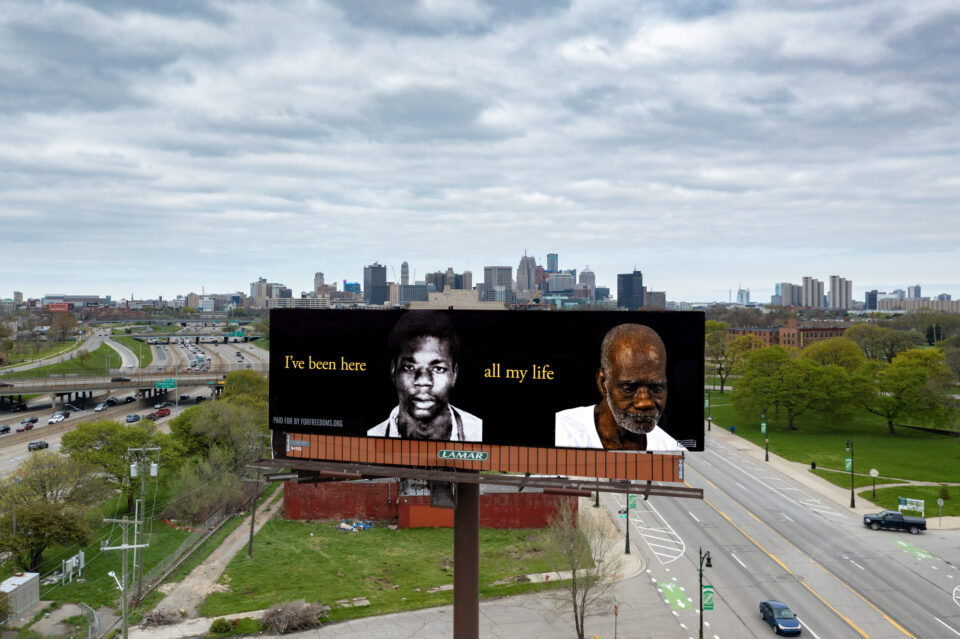 a billboard with side by side photos of a Black man before and during his incarceration. The yellow text reads, "I've been here all my life."